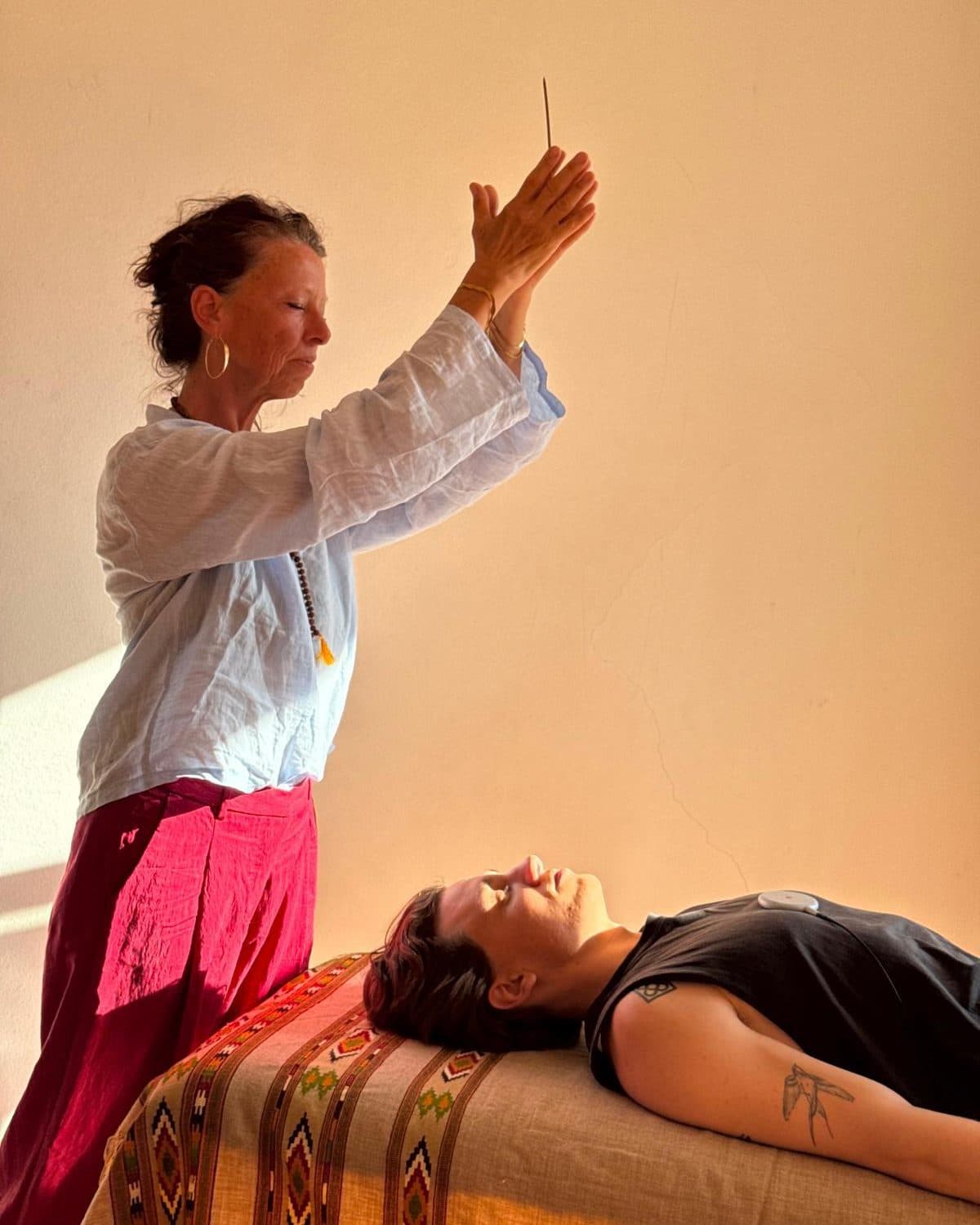Beatrix with raised hands during a frequency session, a client resting on the table